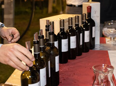 On the table, there are many bottles of Teroldego Rotaliano, a ruby-red wine considered the prince of Trentino wines, along with other white and rosé wines. You can see the hand of the producer taking a bottle to pour it into a participant's glass at the event.